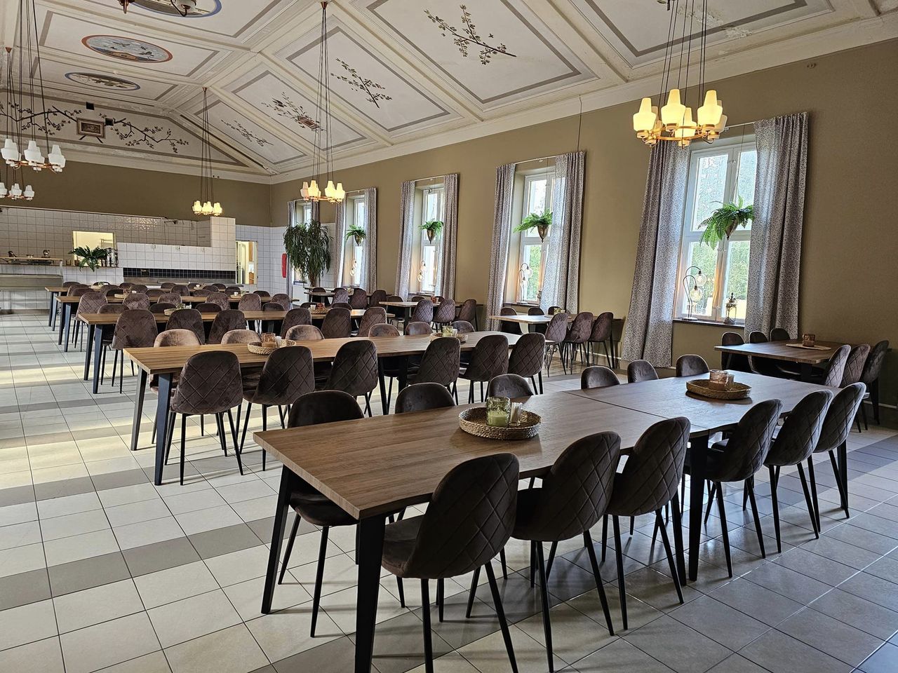 Matsalen med långbord, sammetsstolar, mässingskronor och målade kvistar i taket